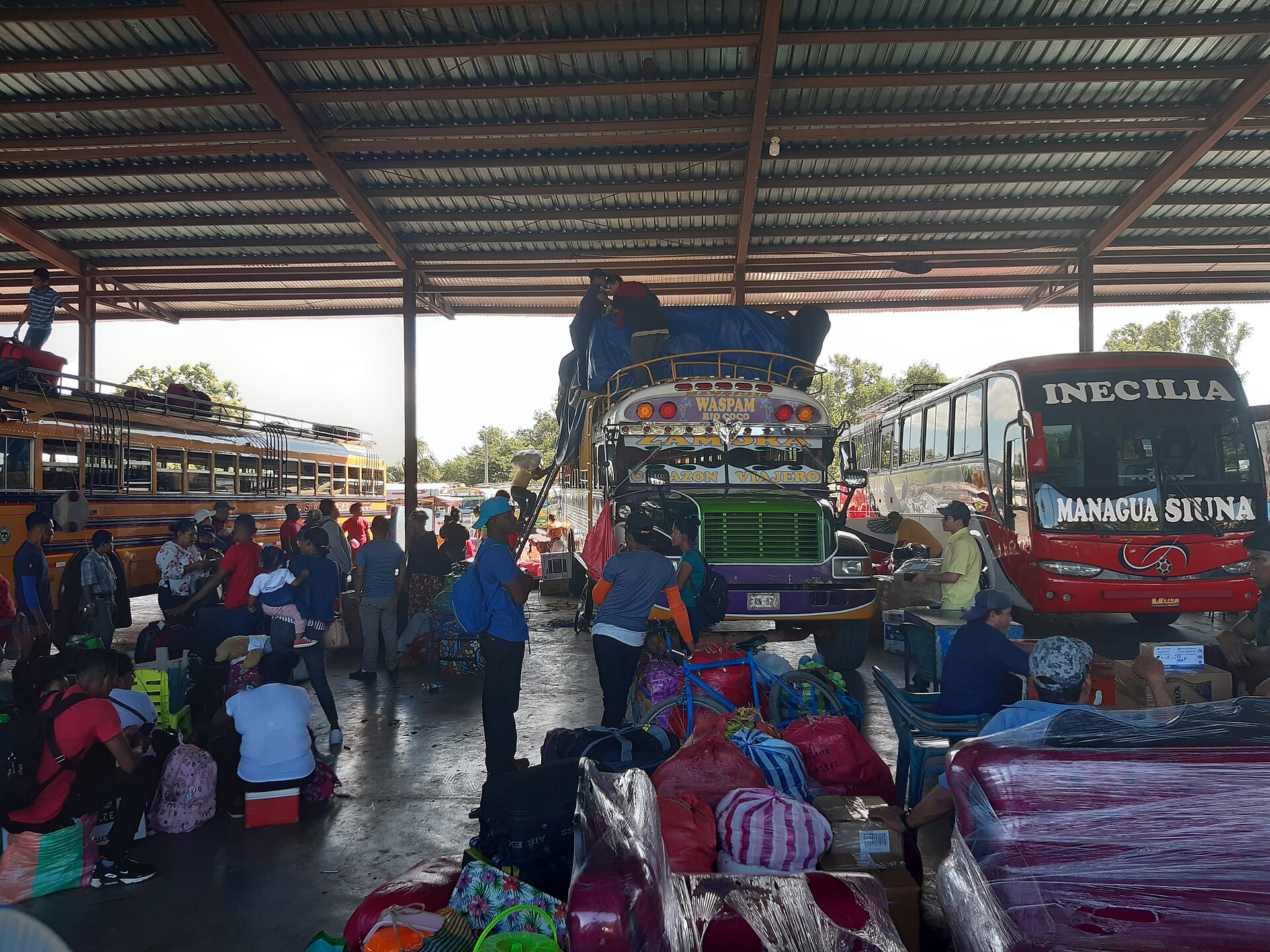Passengers and luggage beside buses at a covered bus station in Managua