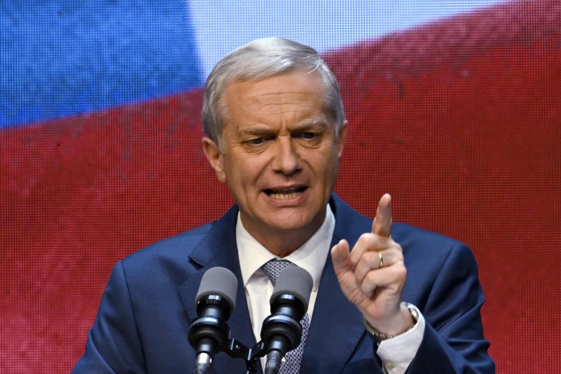 Man speaking at podium with Chilean flag in background