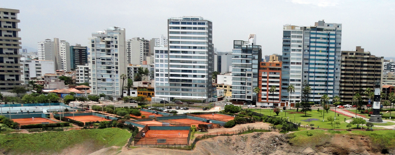 Apartment towers along the clifftop in Miraflores, Lima, with clay tennis courts and a park on the slope below.