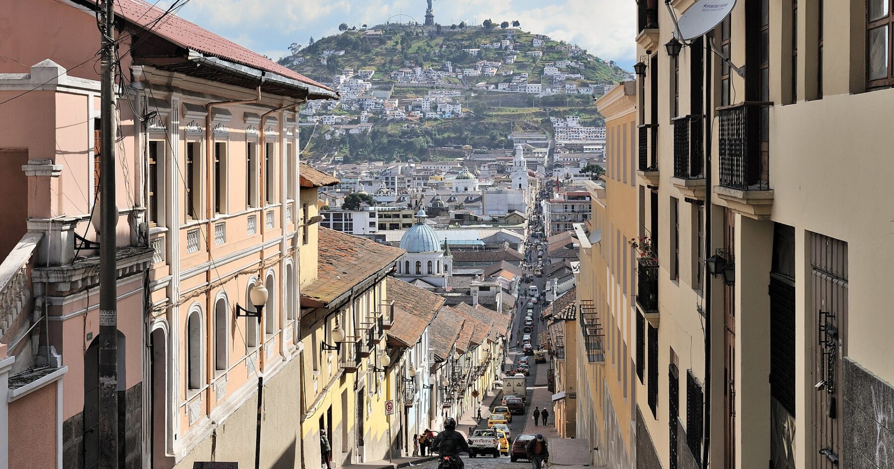 Cobbled García Moreno street in Quito with colonial buildings and El Panecillo hill in the background