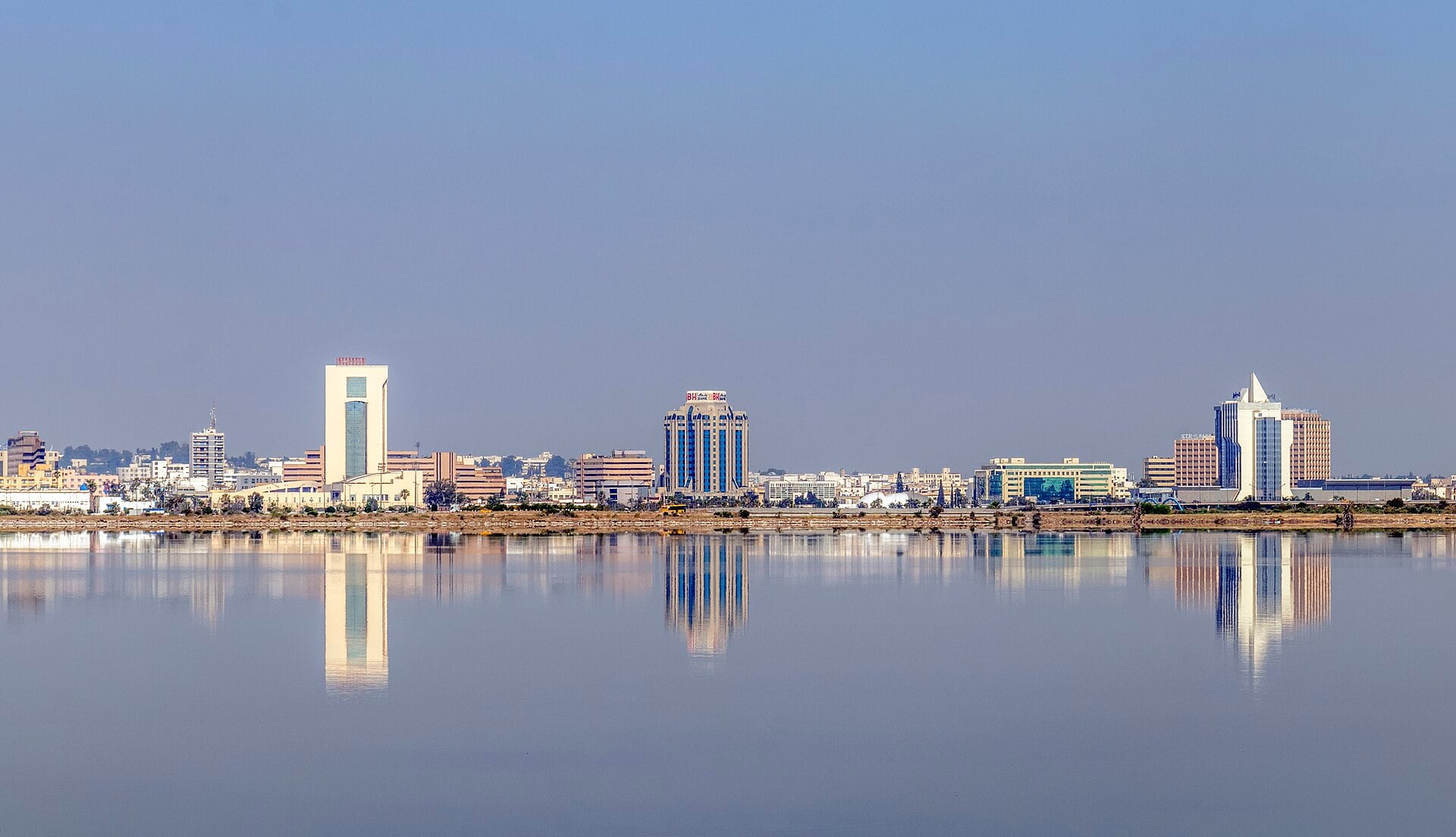 Office towers on the Tunis lakefront reflected in the still water of the Lake of Tunis under a clear sky.