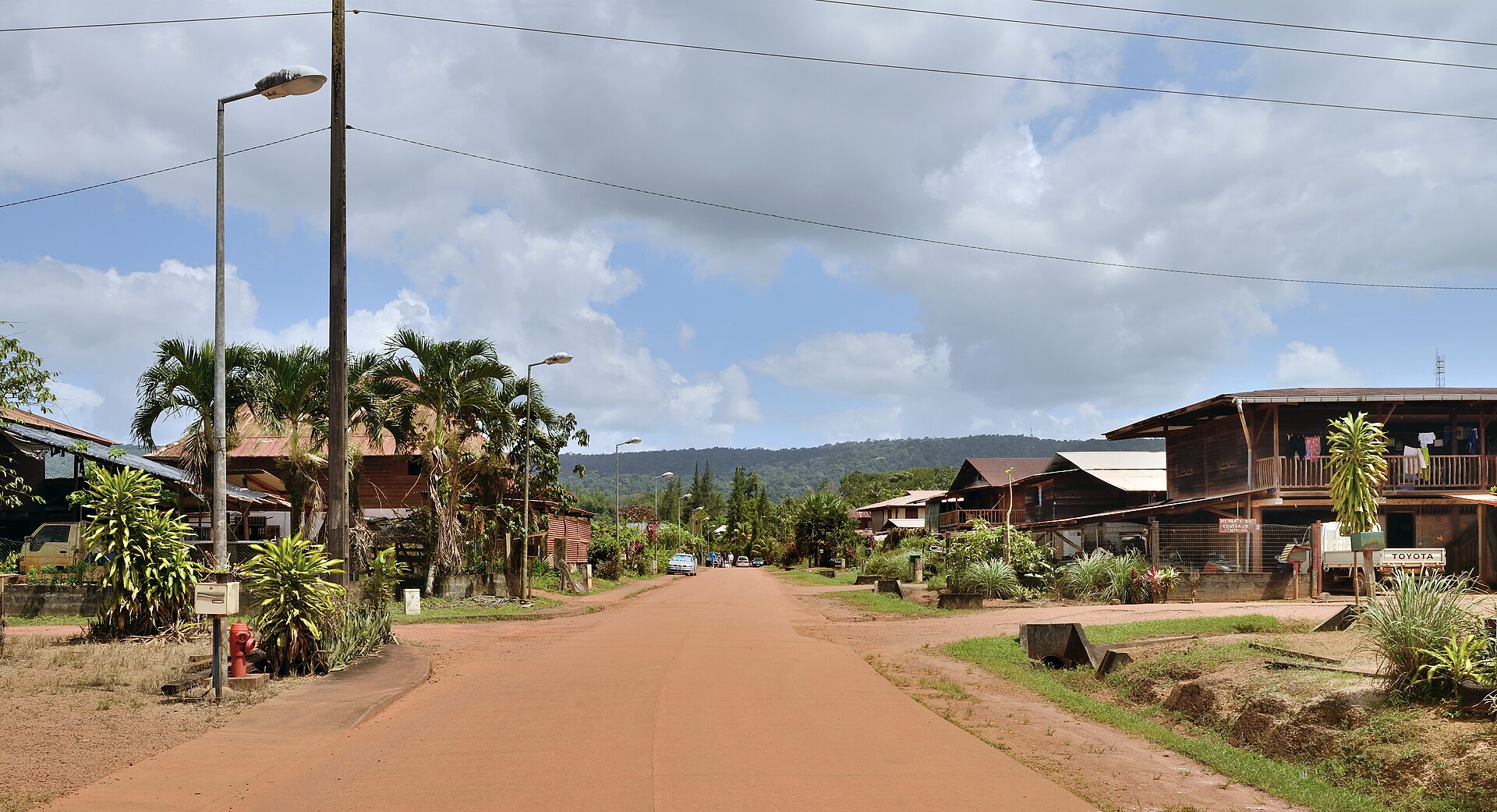 A wide red-earth village street lined with wooden houses on stilts in French Guiana