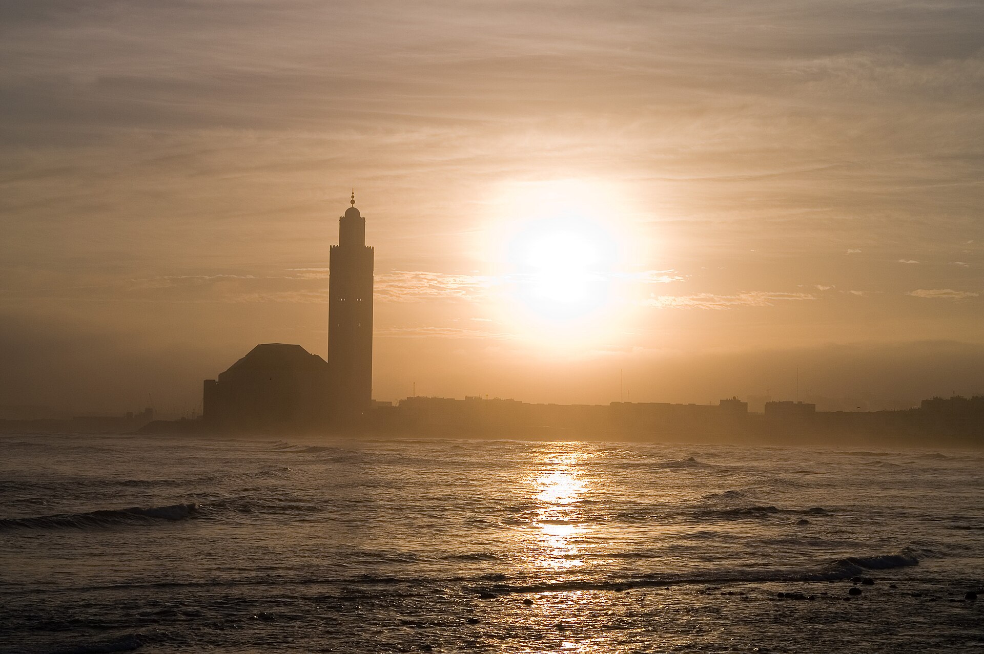 The minaret of the Hassan II Mosque in Casablanca silhouetted against a hazy sunset over the Atlantic.