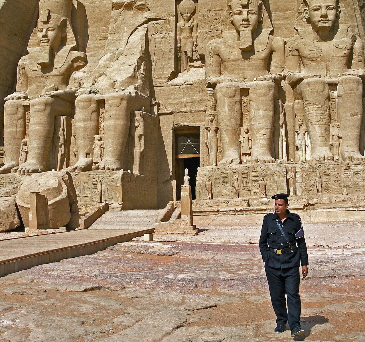 A guard walking past the colossal seated statues at the entrance of the Great Temple of Abu Simbel
