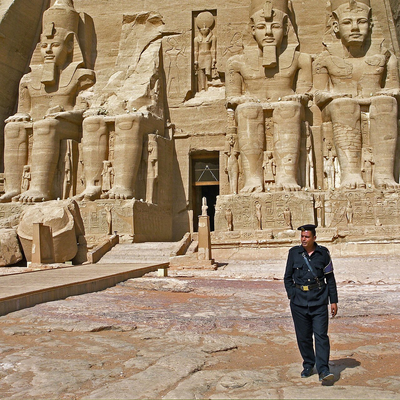 A guard walking past the colossal seated statues at the entrance of the Great Temple of Abu Simbel