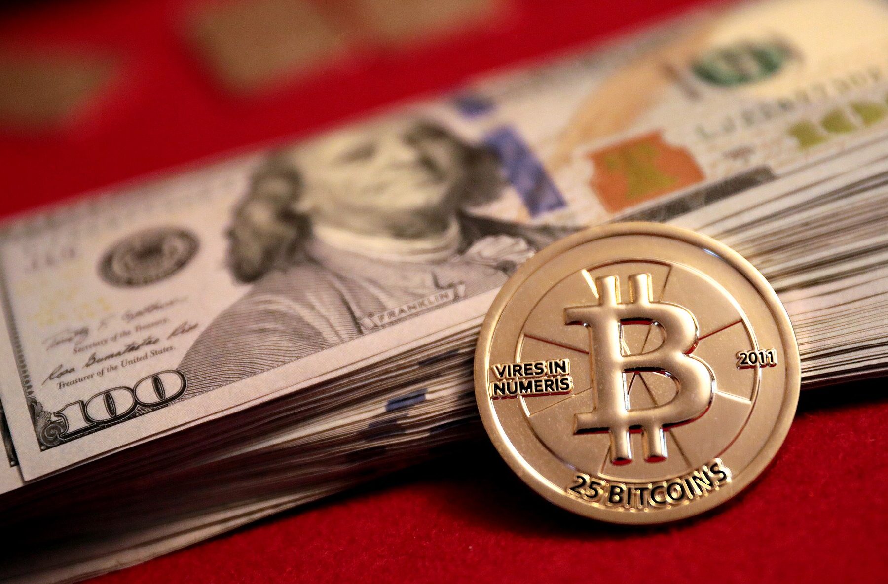 A physical Bitcoin coin resting on a stack of US$100 bills