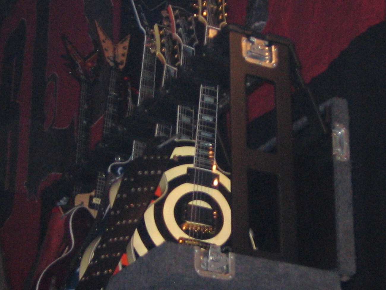 A rack of electric guitars on a darkened stage, including the black and white bullseye Les Paul associated with Zakk Wylde.