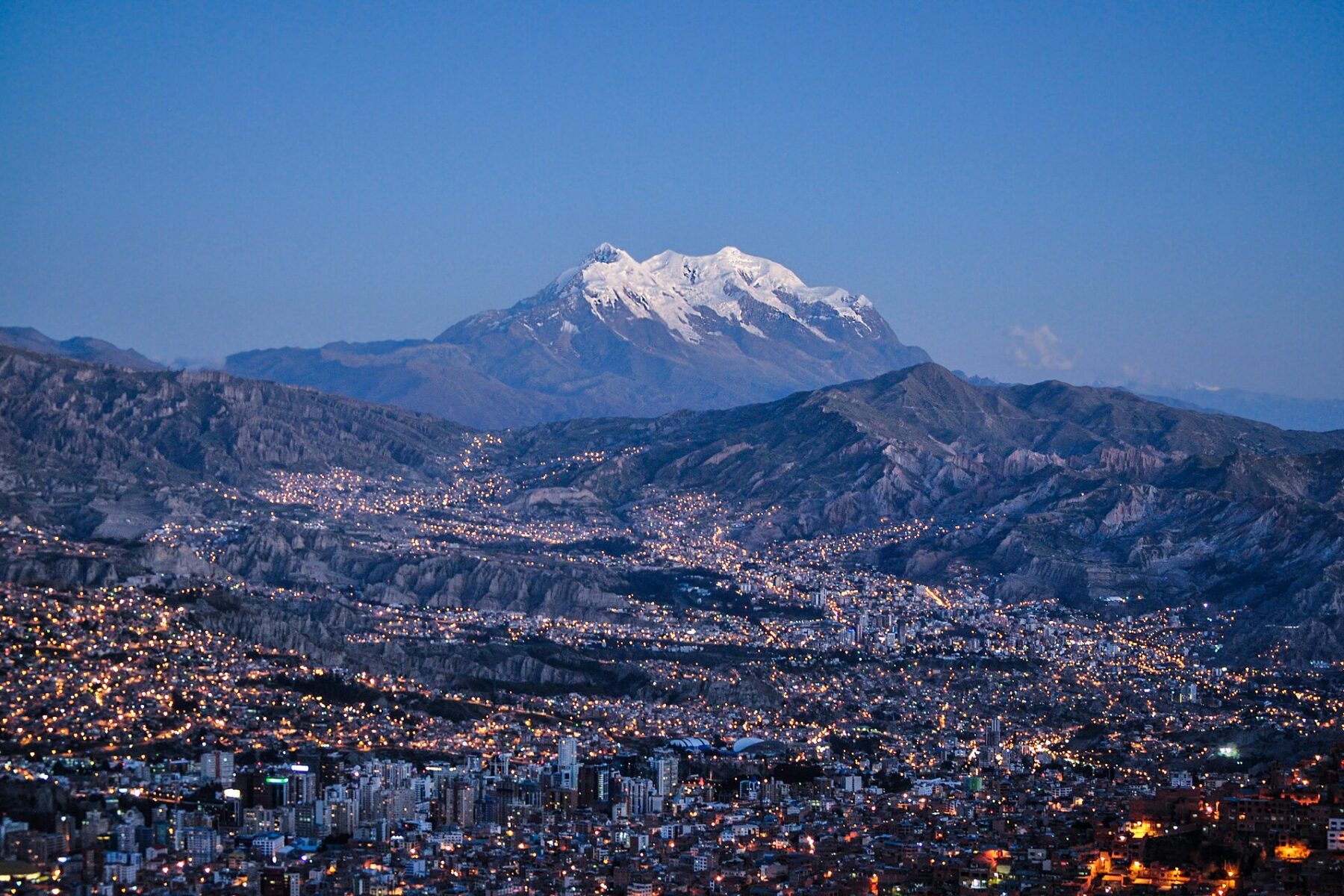 La Paz at dusk with the snow-capped Illimani mountain behind the city lights