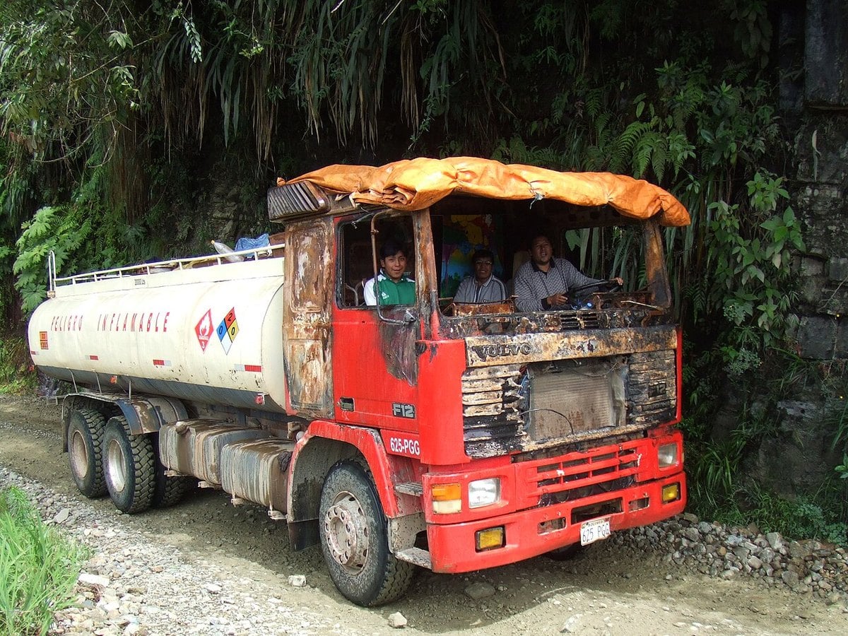 A fuel tanker truck with a fire-damaged cab on a gravel road in the Bolivian Yungas, with its driver and passengers inside