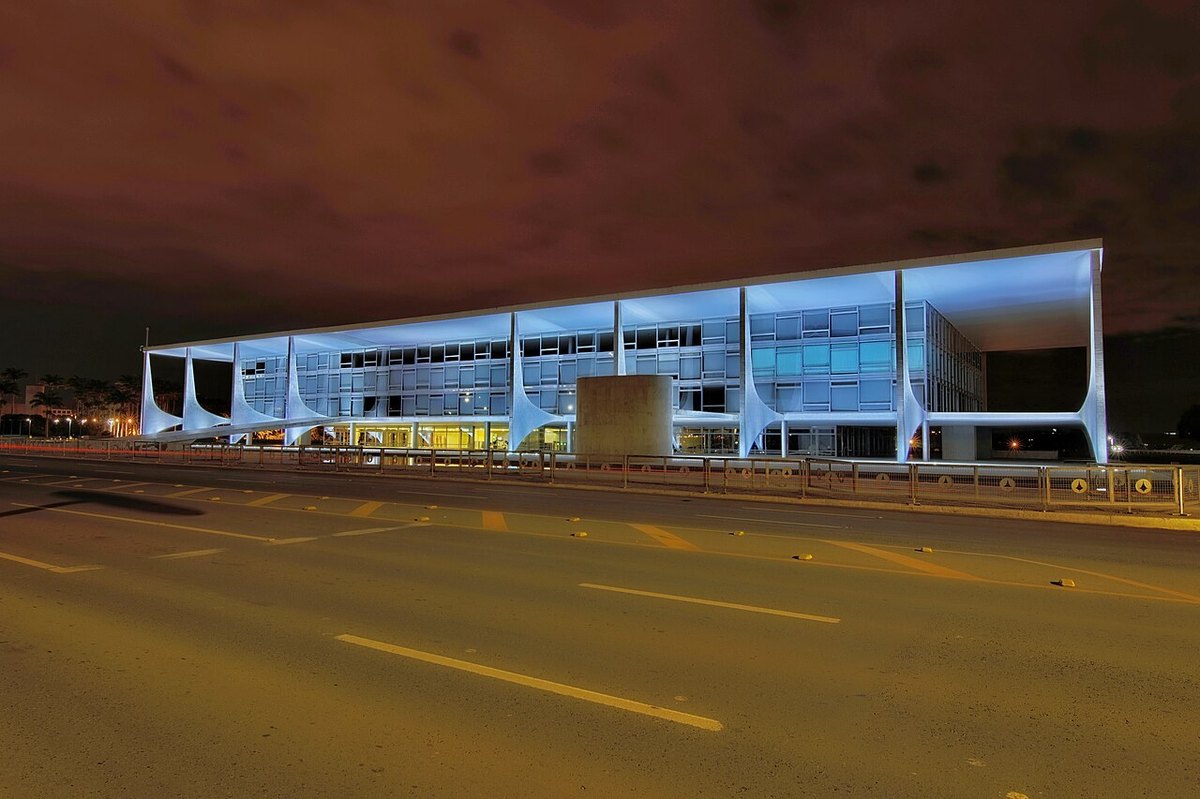 The Planalto Palace in Brasilia lit blue at night, seen from the empty avenue in front of it