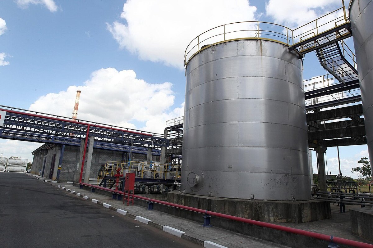 A steel storage tank and pipe racks at a petrochemical plant in Bahia under a blue sky