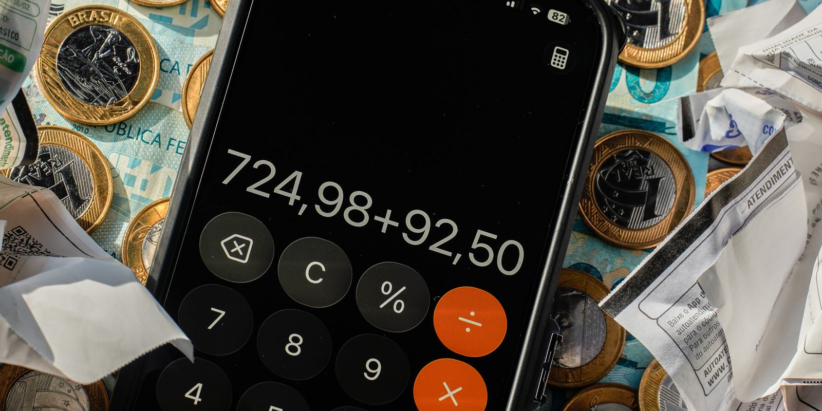 Brazil bank account freeze: a phone calculator adding up bills on top of Brazilian real coins, banknotes and payment receipts