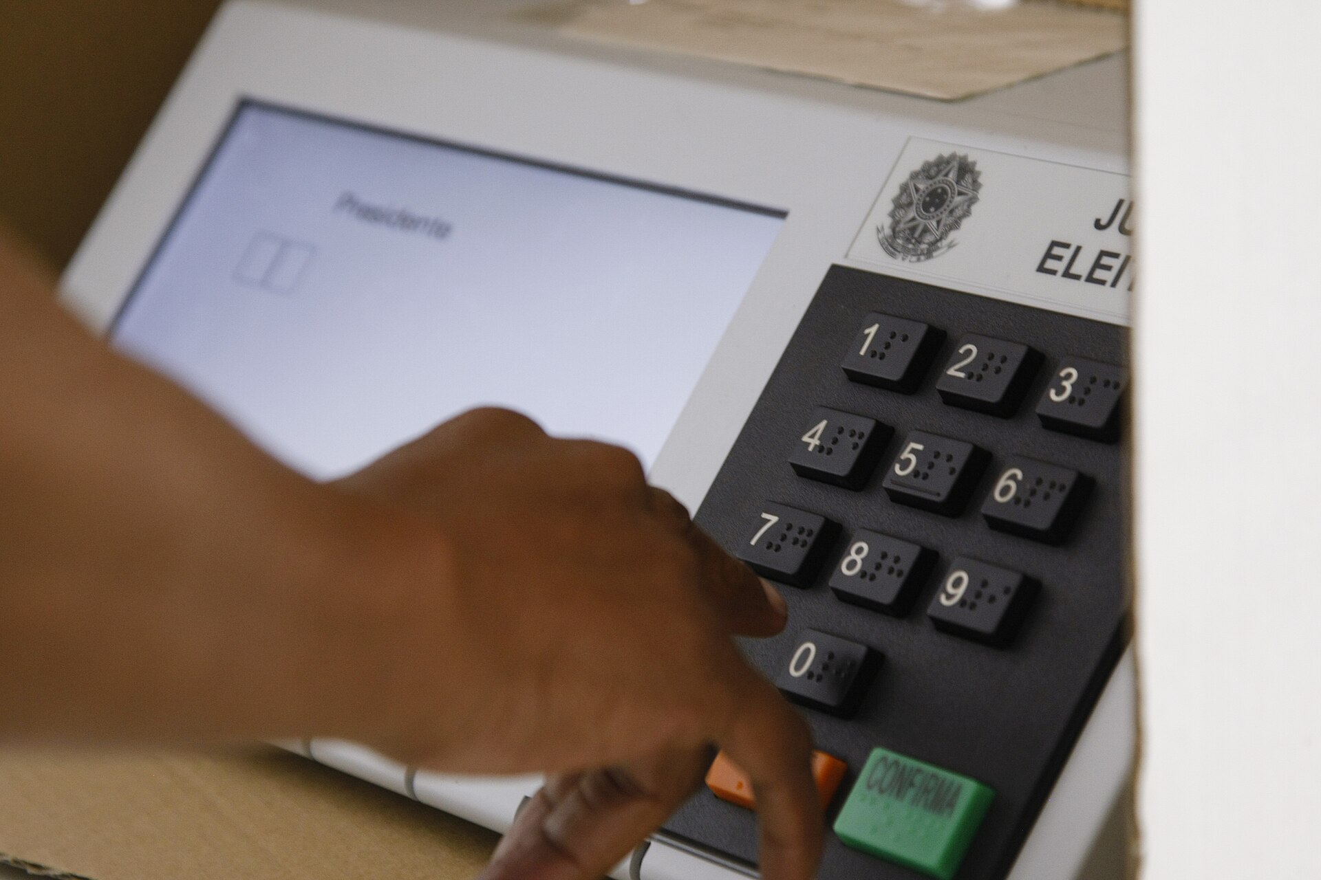 A voter's hand over the keypad of a Brazilian electronic voting machine showing the presidential ballot screen