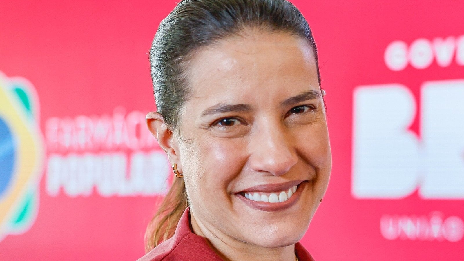 Pernambuco governor Raquel Lyra smiling at a public event in Recife in front of a red backdrop