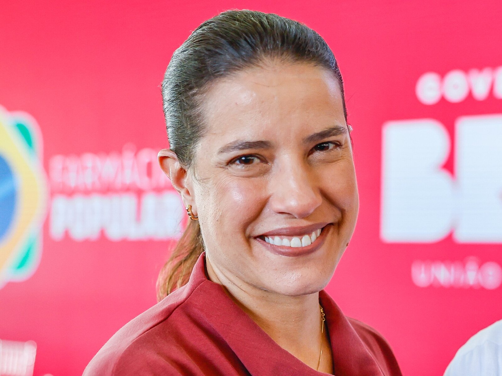 Pernambuco governor Raquel Lyra smiling at a public event in Recife in front of a red backdrop