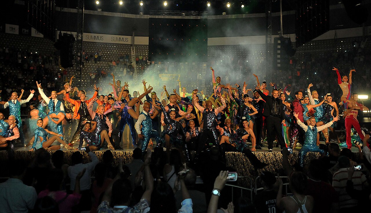 A large group of costumed salsa performers cheering on stage under stage lights at a past World Salsa Festival show in Cali