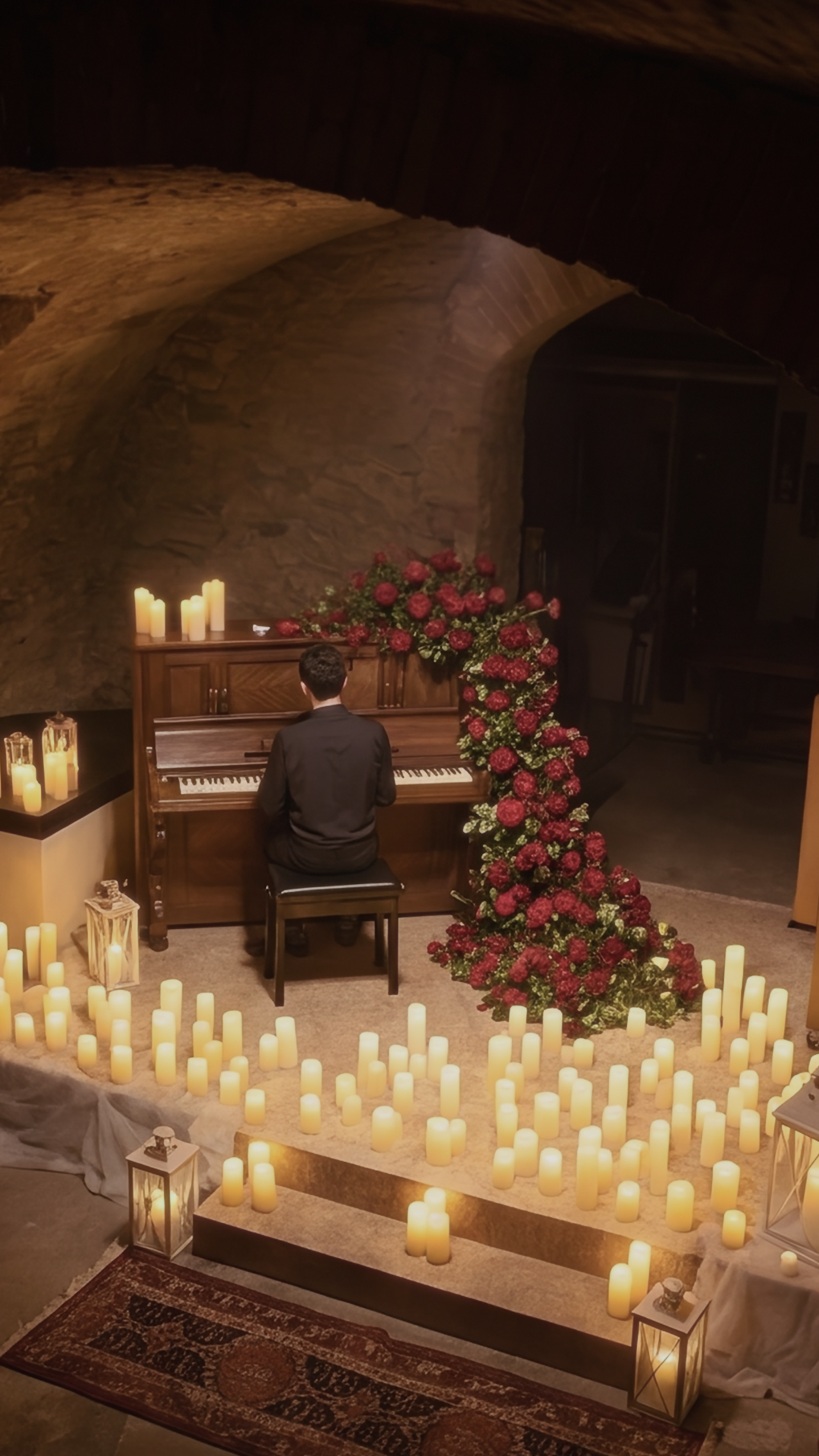A pianist performs surrounded by rows of lit candles at a candlelight-format concert.