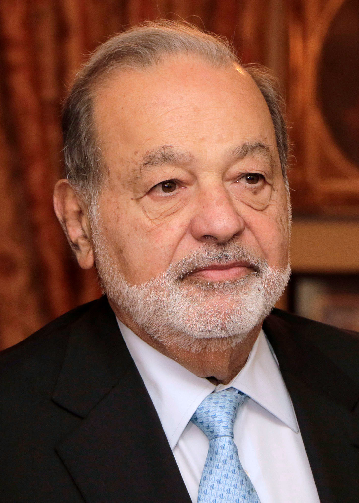 Close-up portrait of Carlos Slim, an older man with white hair and a white beard, wearing a dark suit and light blue tie