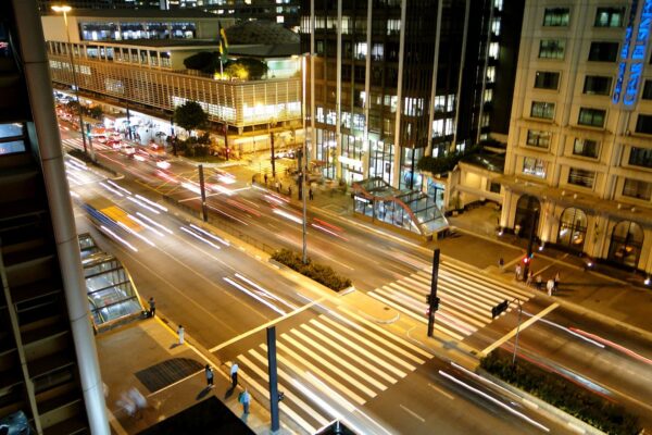 The Conjunto Nacional building lit up at night on Avenida Paulista, with light trails from traffic, pedestrian crossings and a glass-roofed metro entrance
