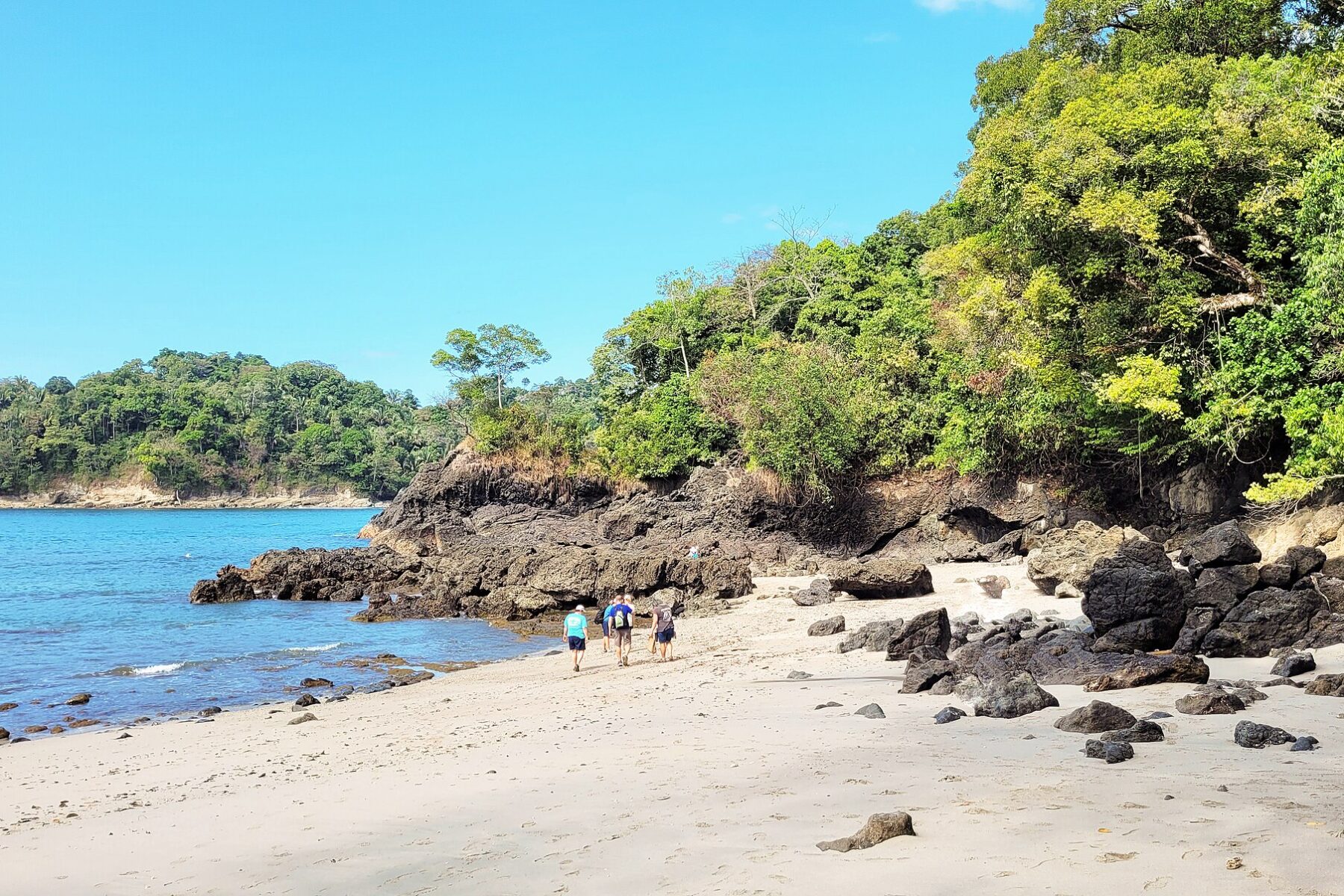 Costa Rica ecotourism — hikers on a beach below the forest in Manuel Antonio National Park