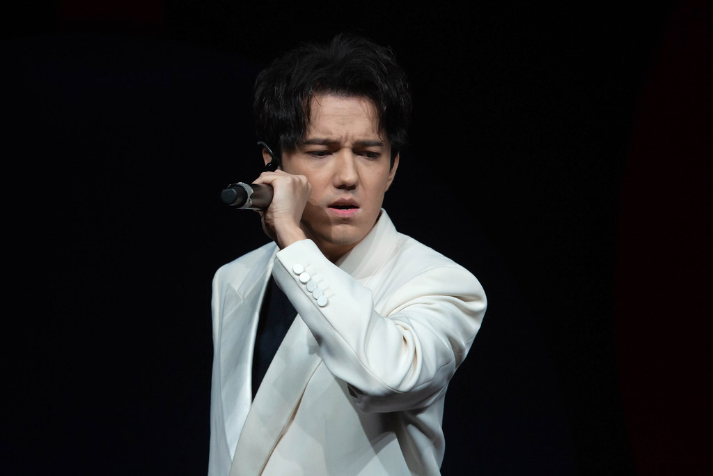 Dimash Qudaibergen in a white suit singing into a microphone, ahead of the Dimash Bogotá concert