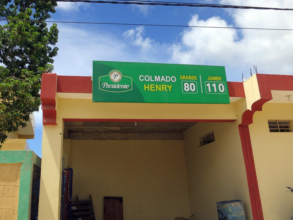 Yellow and red single-storey corner shop under a green sign reading Colmado Henry, with an open, empty storefront