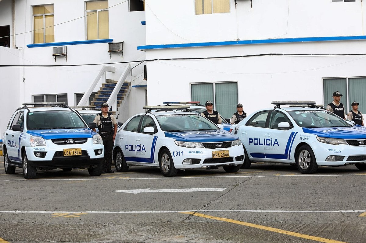 Ecuadorian National Police officers standing beside marked patrol cars outside a police station