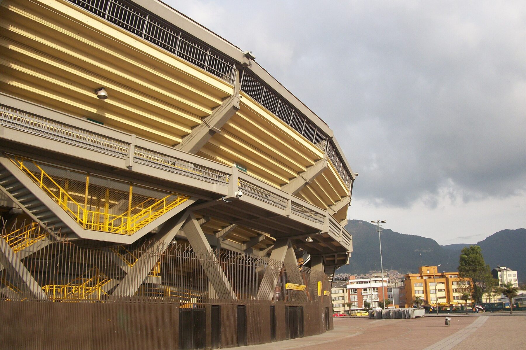 The exterior of Estadio El Campín in Bogotá, with its concrete stands and yellow railings and the mountains behind.