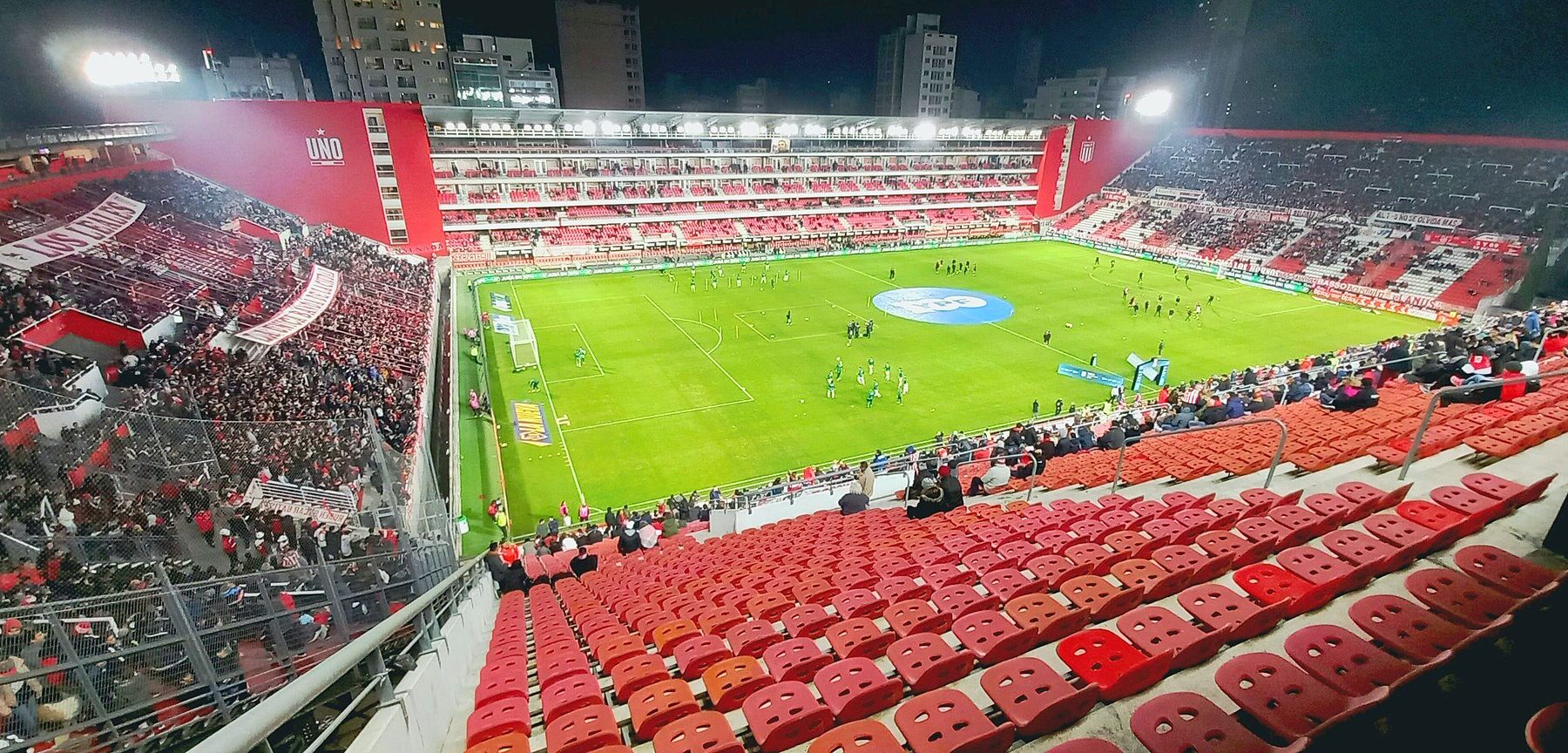 Estudiantes de La Plata's Estadio UNO lit up at night before a match, with red seats and packed stands