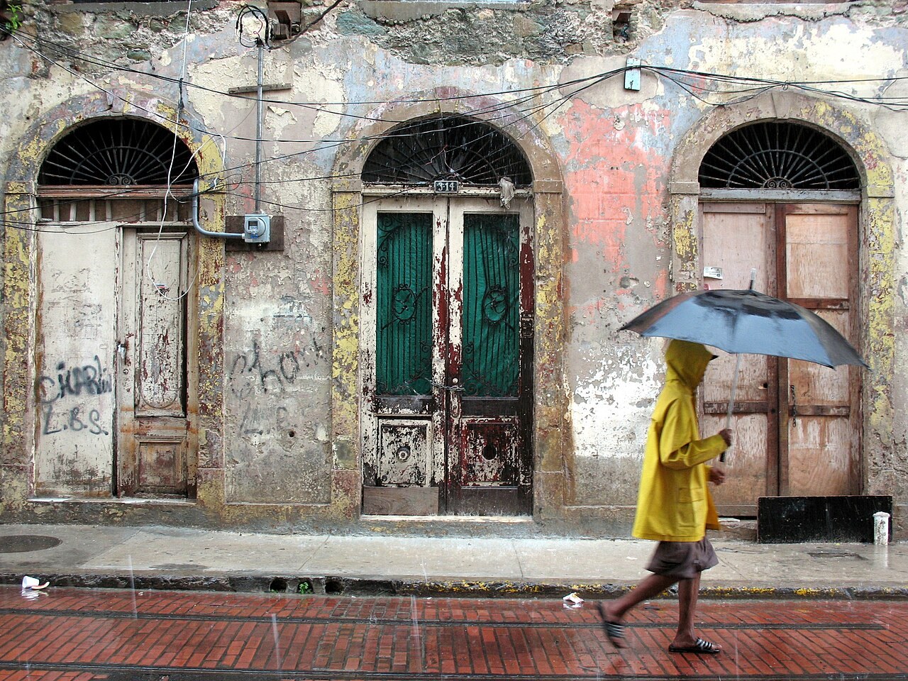 Federico Suárez - Pedestrian with an umbrella on a brick-paved street before old doorways in the Casco Antiguo
