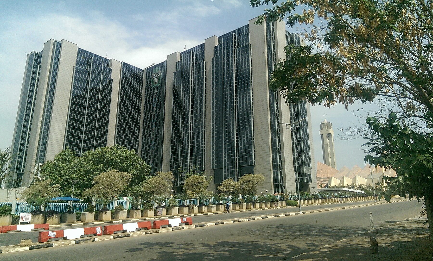 The Central Bank of Nigeria headquarters building in Abuja, seen from a tree-lined avenue.