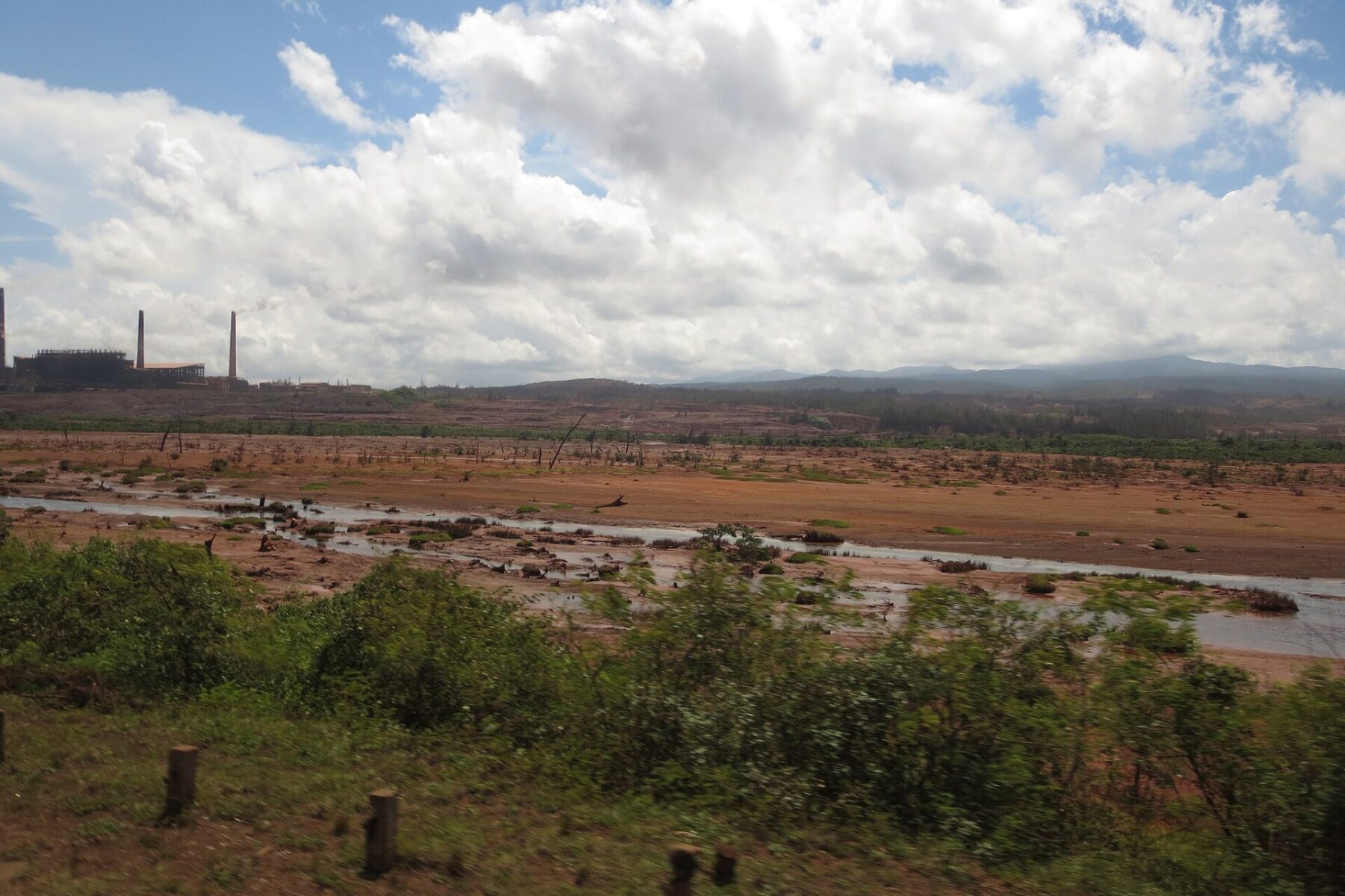 Red earth of a nickel mining area near Moa in eastern Cuba, with processing plant chimneys on the horizon