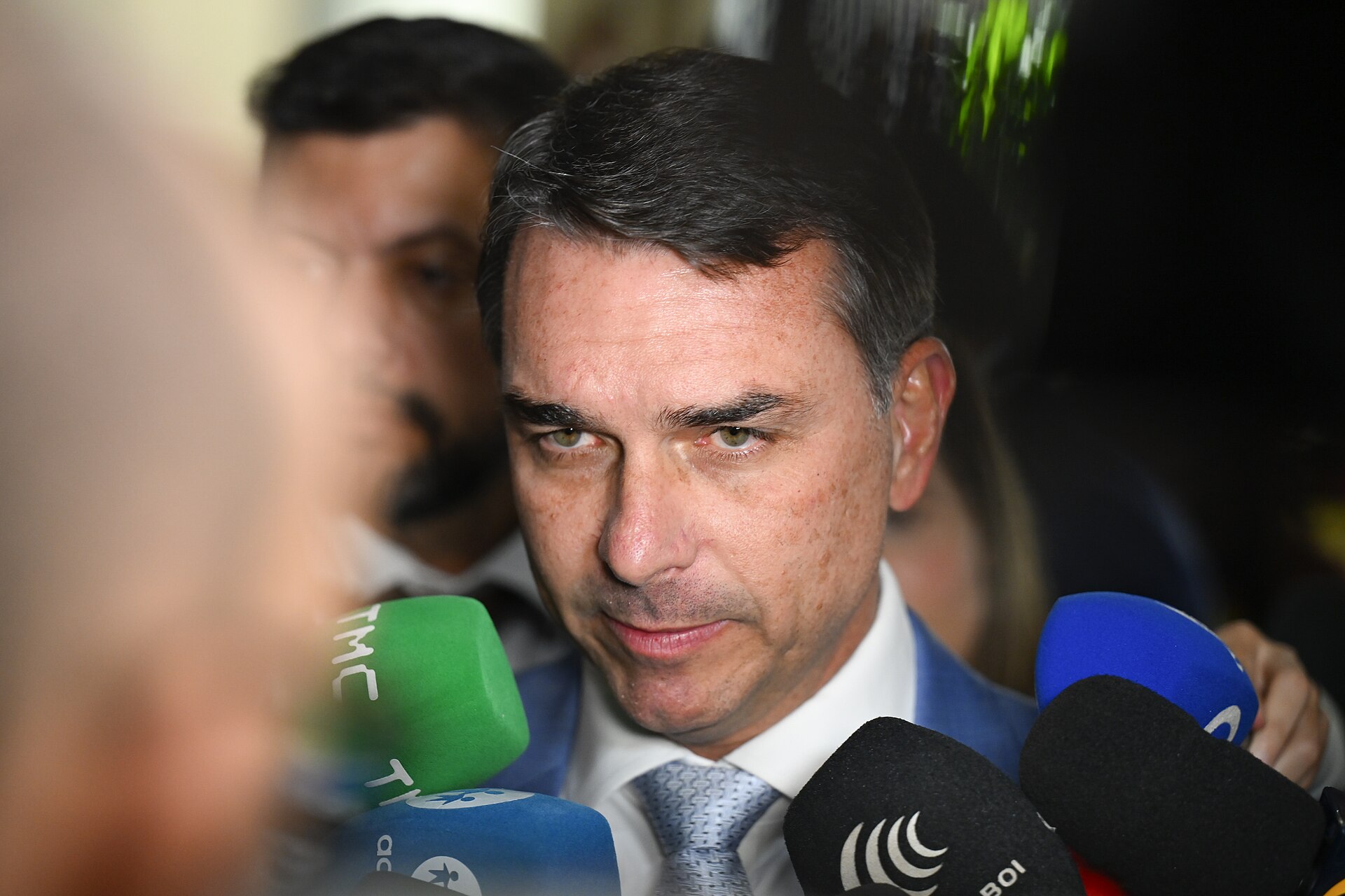 Senator Flávio Bolsonaro speaking to reporters surrounded by microphones