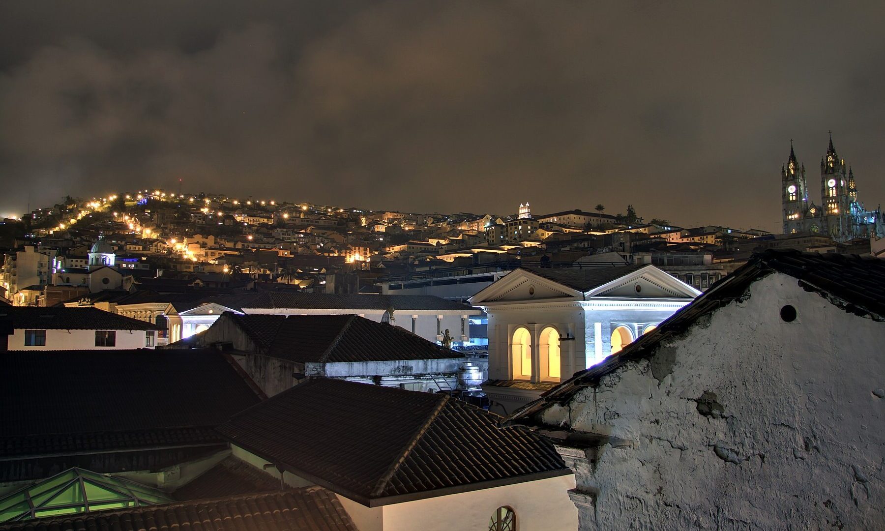 Rooftops of Quito's historic centre at night, with the lit towers of the Basílica del Voto Nacional, the city of the Grupo Frontera Quito concert on 9 October 2026