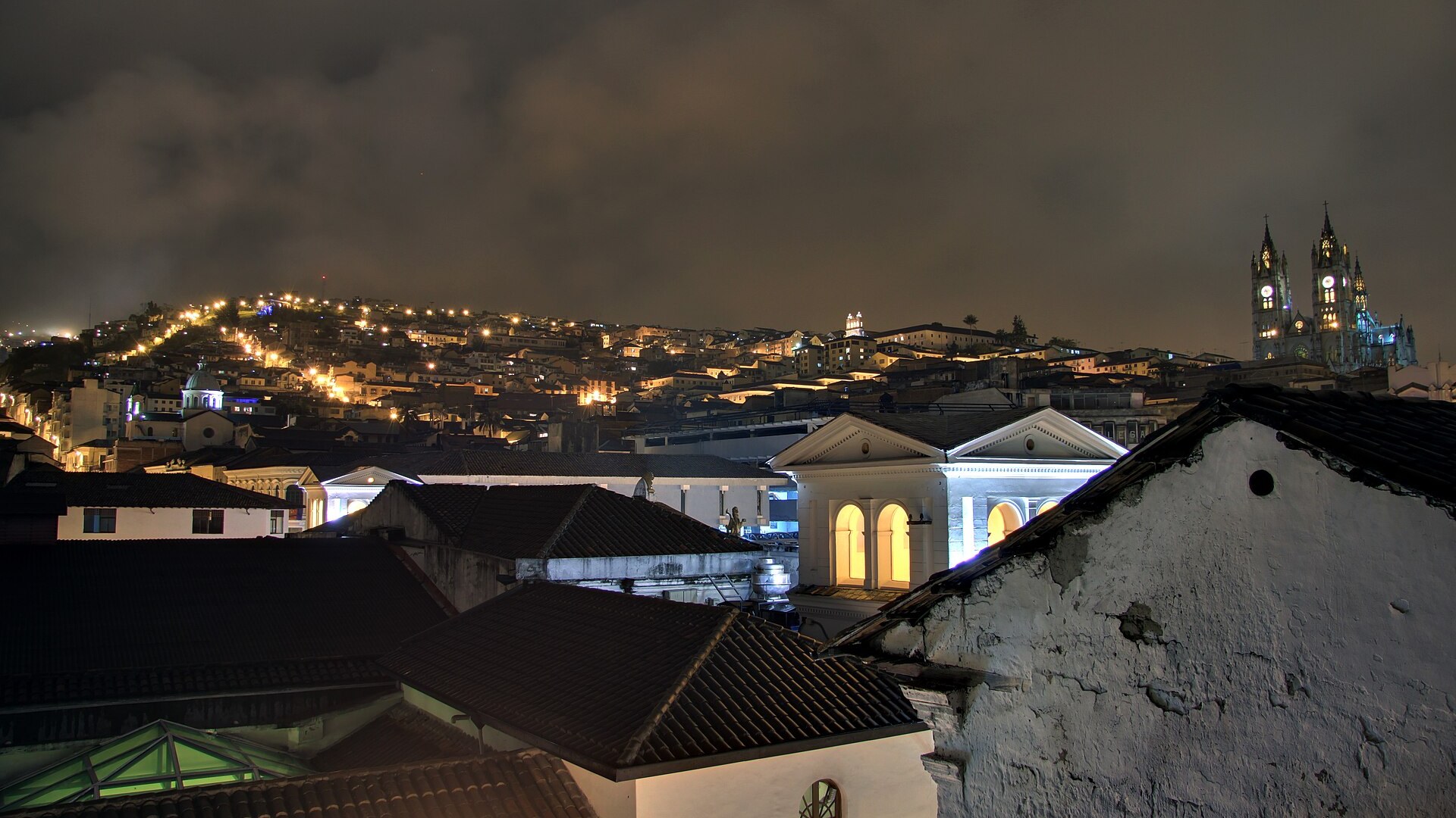 Rooftops of Quito's historic centre at night, with the lit towers of the Basílica del Voto Nacional, the city of the Grupo Frontera Quito concert on 9 October 2026