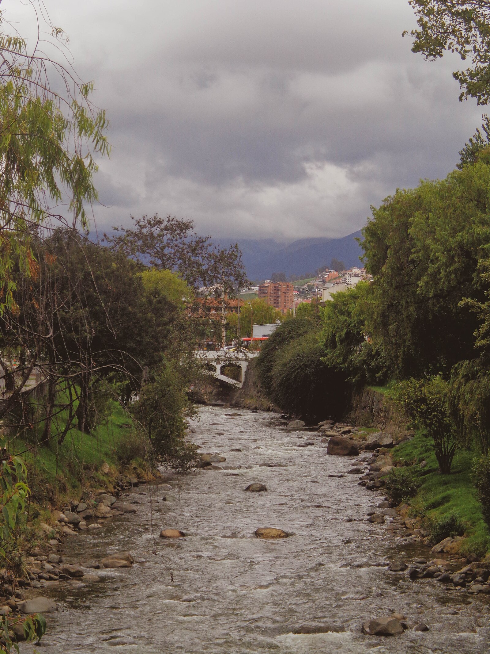 The Tomebamba river flowing through Cuenca, Ecuador, with the city rising behind it