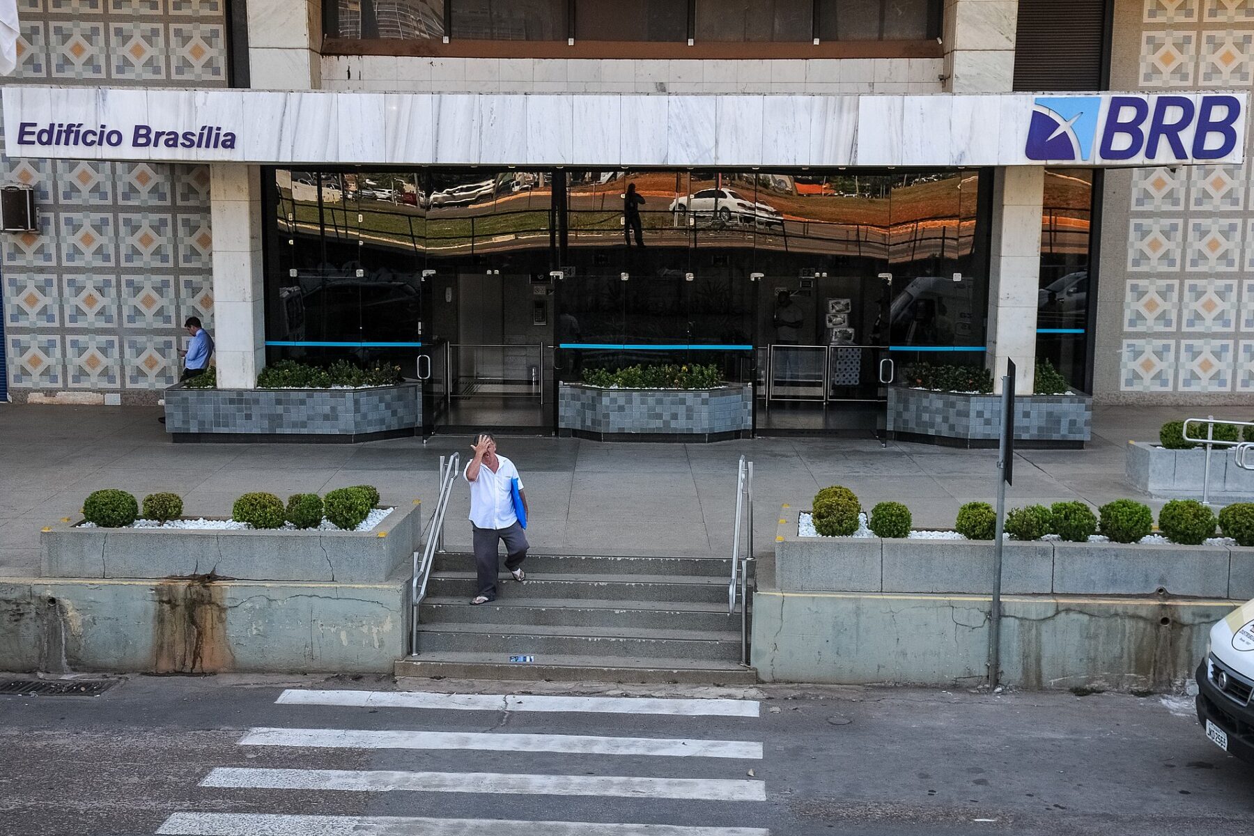 A man holds his head as he walks down the steps outside a BRB bank branch entrance in Brasilia