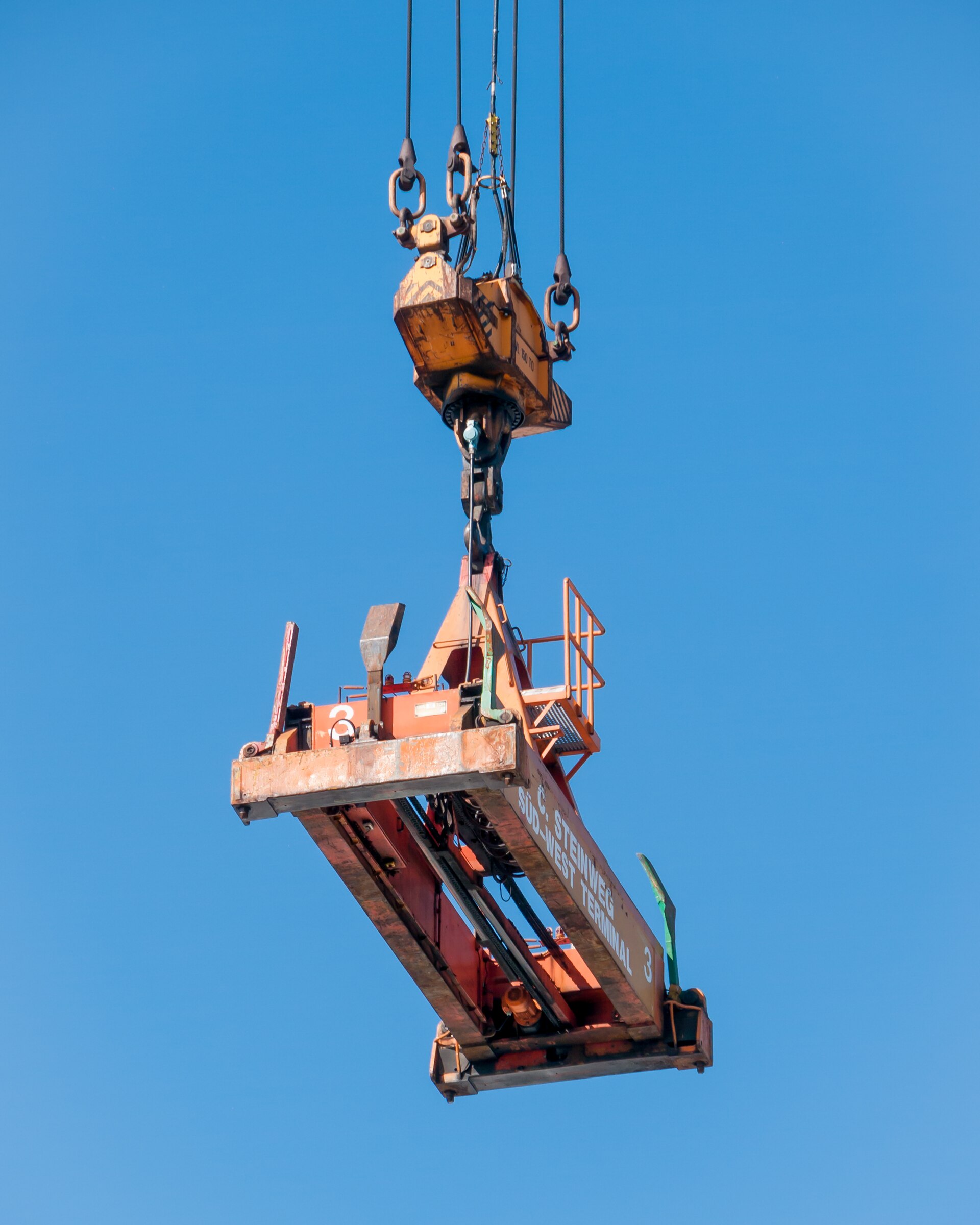 A container crane spreader suspended against a clear sky