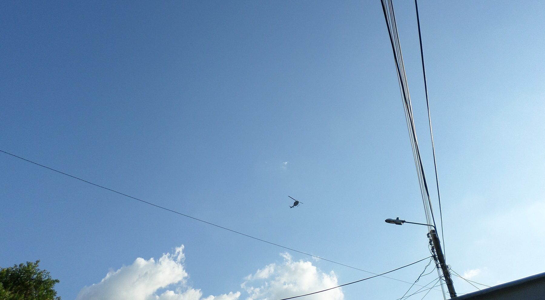 A helicopter in the distance over power lines and a street lamp against a blue sky in Colombia