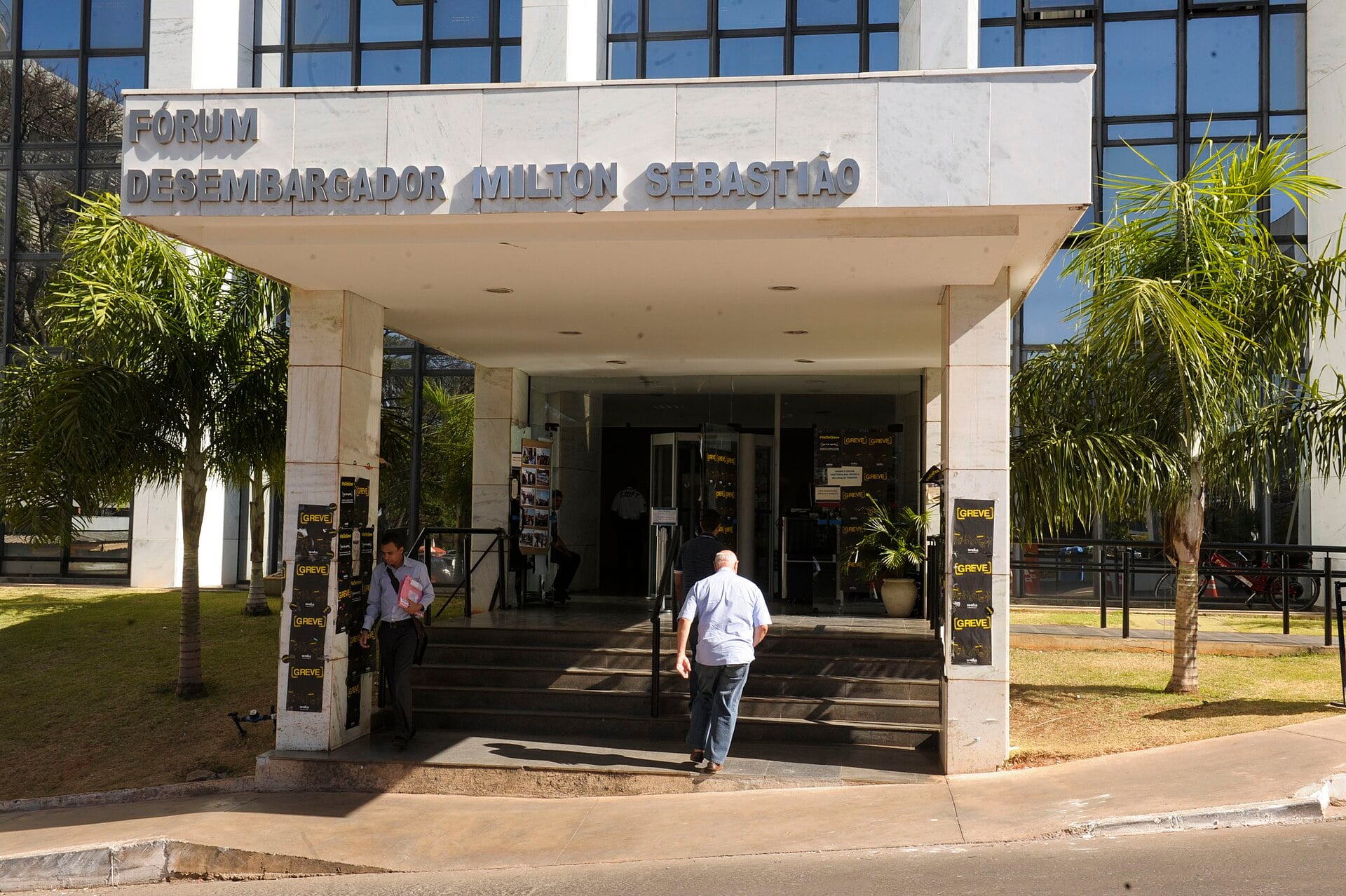 Lawyers walking in and out of a marble courthouse entrance in Brazil's Federal District under a bright sky
