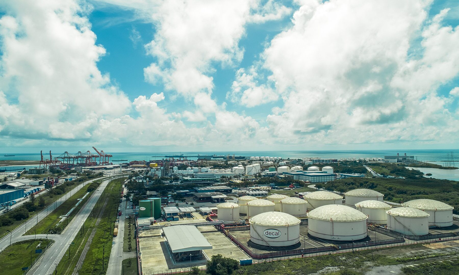 Aerial view of white fuel storage tanks and container cranes at the Suape port complex on the Brazilian coast