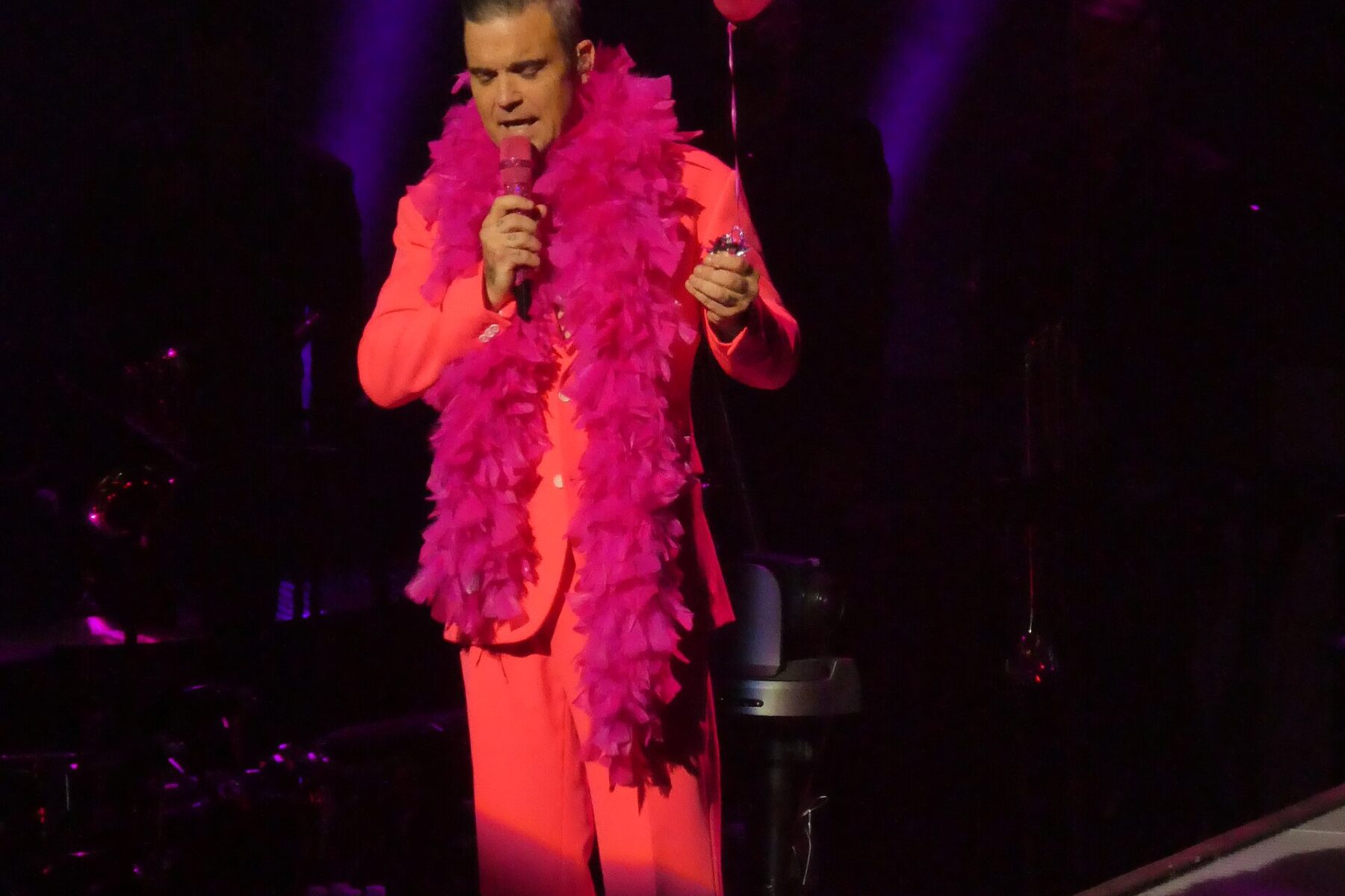 Man in pink boa and suit holding microphone