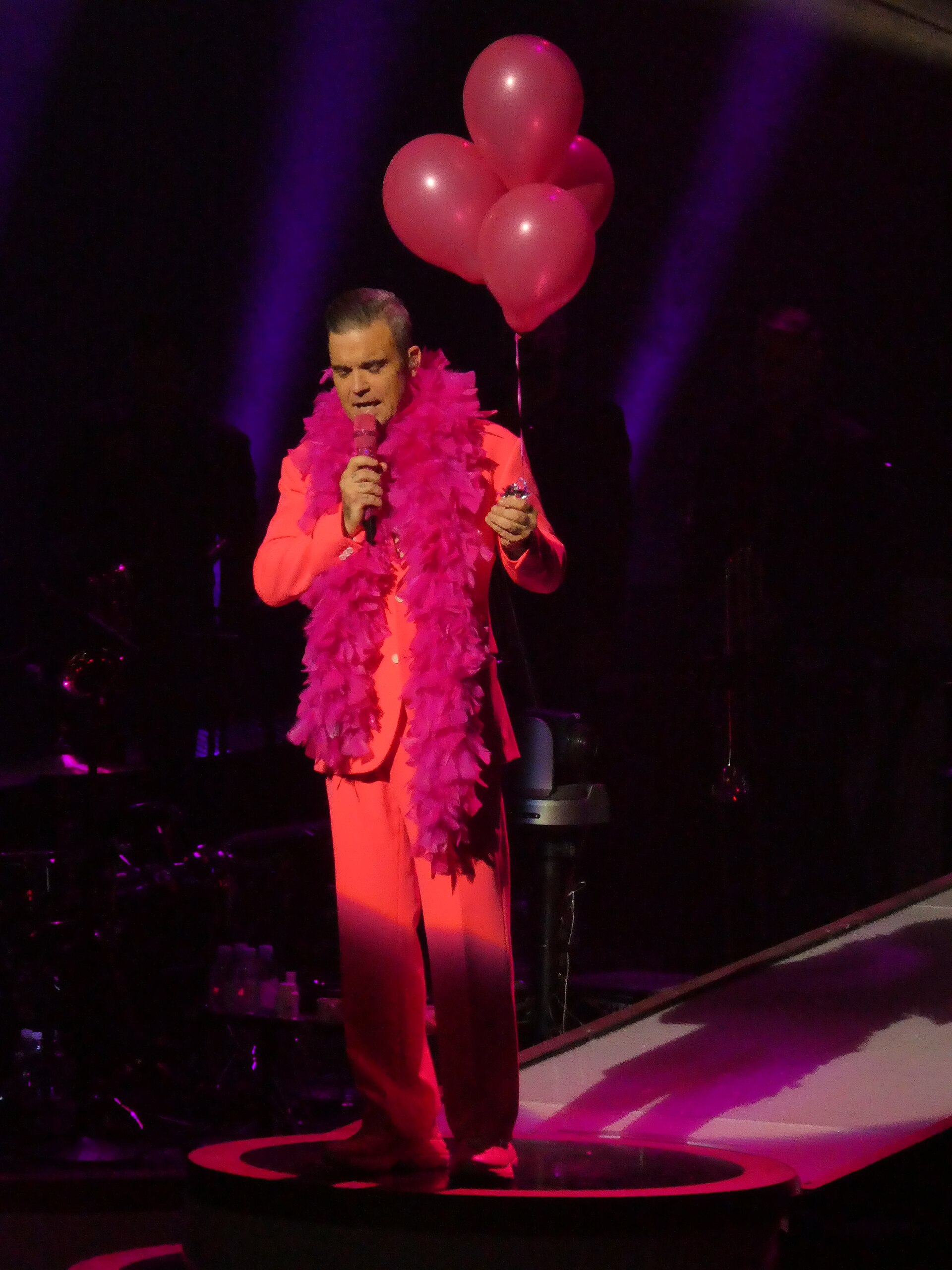 Robbie Williams performing on stage holding balloons