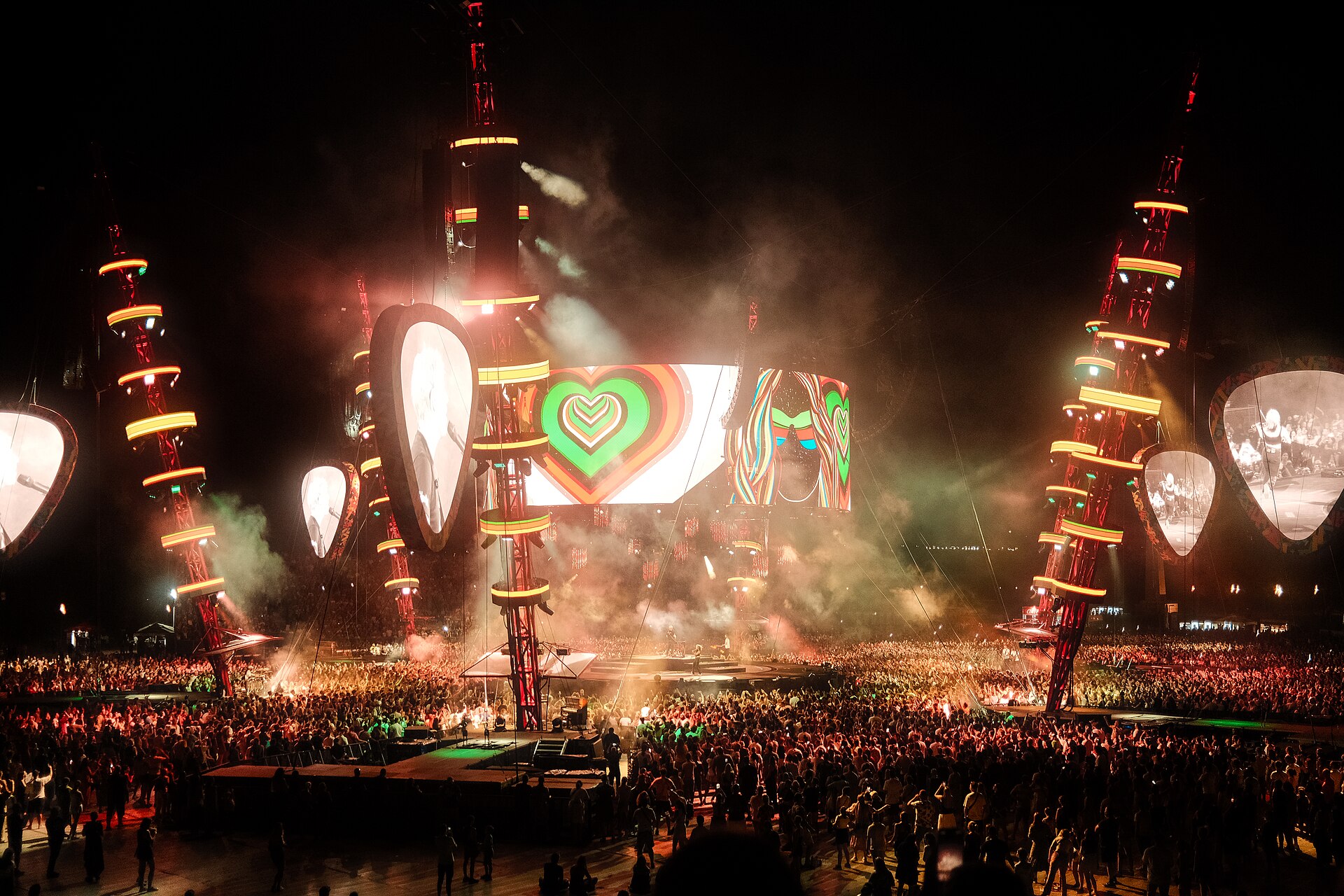 A large outdoor concert stage with heart imagery above a crowd