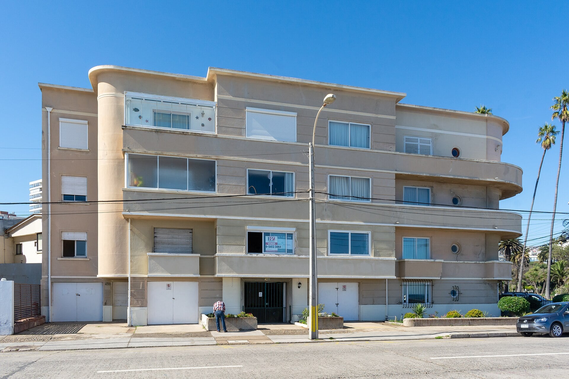A three-storey cream-coloured apartment building in Chile with a for-sale sign in one window and a man standing at the entrance