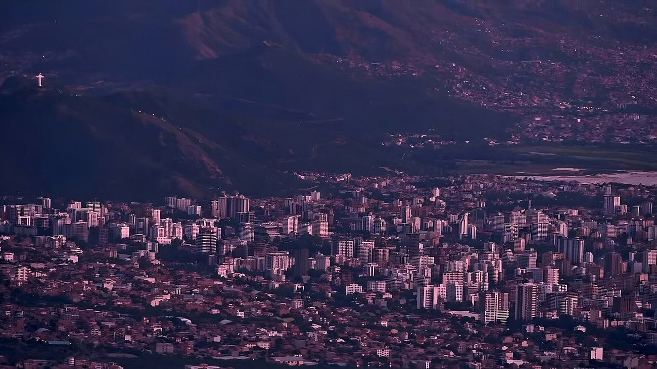 Cochabamba at dusk, seen from above, with the Cristo de la Concordia statue on the hillside at left.