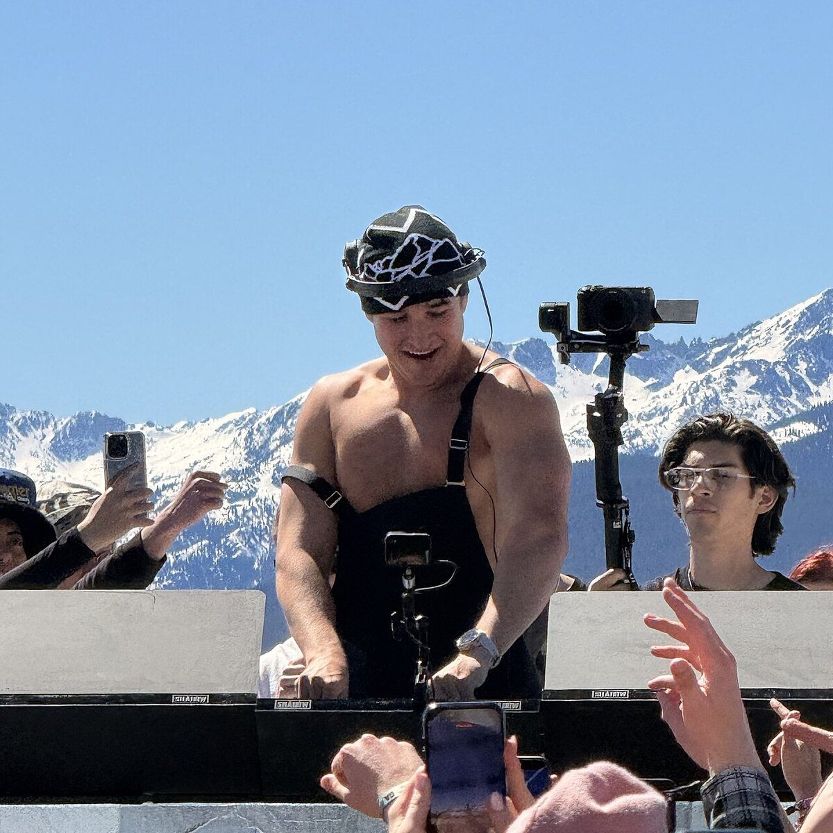 John Summit playing a daytime open-air set with snow-covered mountains behind him