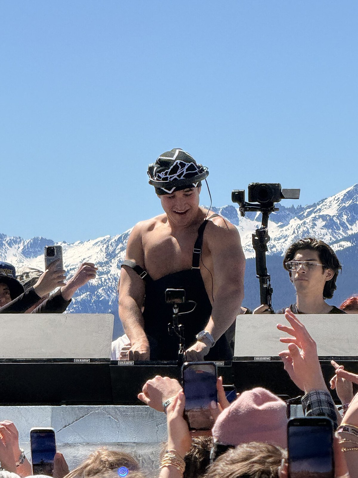 John Summit playing a daytime open-air set with snow-covered mountains behind him
