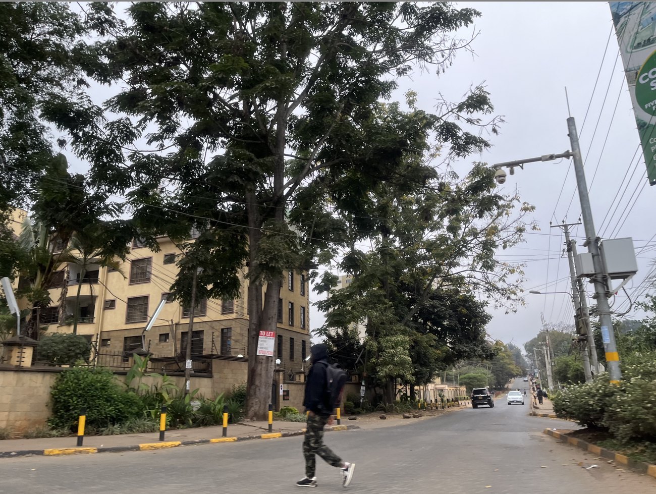 A quiet tree-lined street in the Westlands district of Nairobi, with apartment blocks, a to-let sign and a person crossing the road.