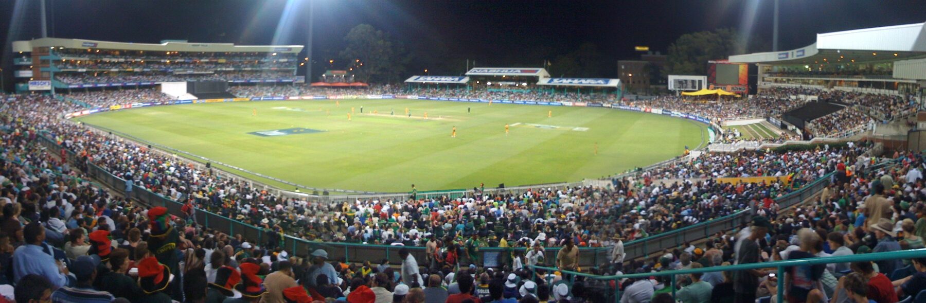 Kingsmead cricket ground in Durban at night under floodlights, the stands full and fielders in yellow spread across the outfield.
